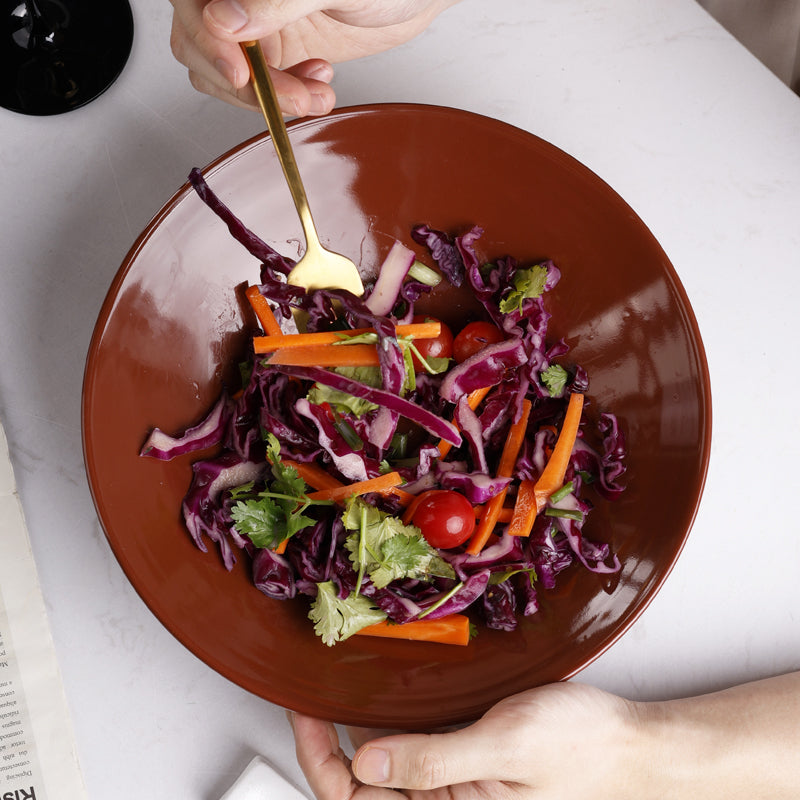 A deep brownish-red ceramic plate with salad